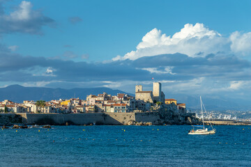 Fototapeta premium View of the rampart walls and the old town of Antibes with a sailboat on the French Riviera in the South of France.