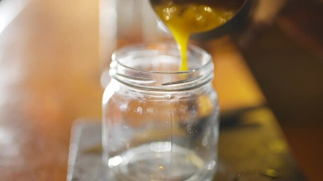 A jar is sitting on a table with a person's hand on it. The jar is empty and the table is made of wood