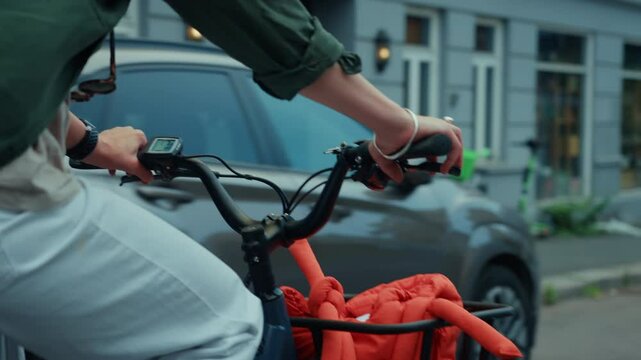 Close up on basket of a cargo electric city bike, handlebar, breaks and gear shifters, basket with stylish orange designer bag. Woman cycle through town on a daily commute