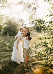 A joyful mother plays with her two children in a sunlit meadow on summer day