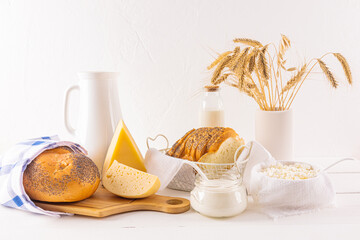 Many varieties of cheese on a board, bottles of milk, cottage cheese, sour cream, a bunch of ears of bread on a wooden table. The holiday of Shavuot.