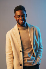 Handsome African American man smiling, dressed in a stylish beige coat and light sweater, against a soft blue background, representing confidence and fashion