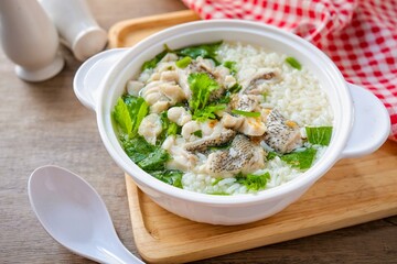 Rice soup with fish in white bowl on wooden background