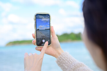 海を眺めながら写真を撮る女性