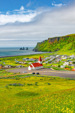 Cover page with basalt stacks Reynisdrangar and yellow meadow flowers at Vik town with Myrdal church, Iceland, at summer sunny day and blue sky.