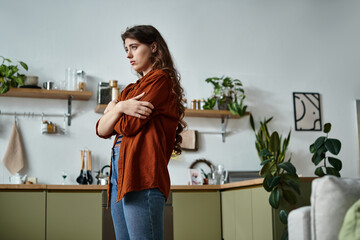 Woman standing alone in a cozy kitchen reflecting on her emotions and feelings of sadness