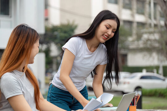 Diverse university students engaging in a study session outdoors with documents and a laptop.
