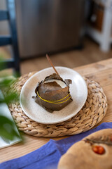 A handmade goat cheese wrapped in fig leaves and tied with twine, presented on a ceramic plate for a rustic gourmet meal. Organic products Craft cheese production using modern technology and affinage 