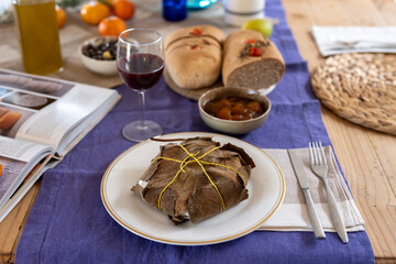 A rustic homemade goat cheese wrapped in fig leaves, served on a set table with bread, chutney, and wine for a gourmet meal. A beautifully set table with farm produce, organic cheeses and wine