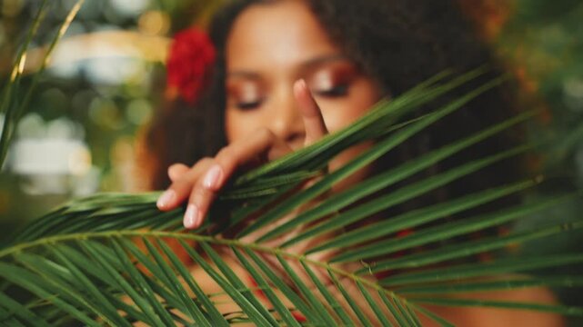 real person happy african woman looking through branch palm leaf green tropical nature. joy fantasy black girl beauty smiling sexy face eyes lips dark hair head shot, savage style make-up spa salon