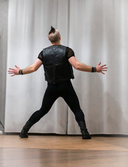 A man in rock clothes performs dance moves. A metal man with a mohawk on his head. Man in motion and gestures of arms and legs in dance.
