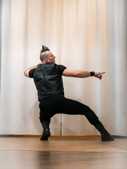 A man in rock clothes performs dance moves. A metal man with a mohawk on his head. Man in motion...