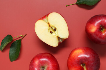 Fresh apples and green leaves on red background, flat lay