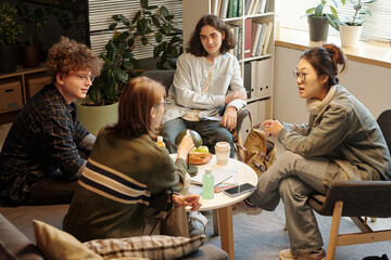 Group of teenage friends enjoying time together chatting and eating snacks round table in college...