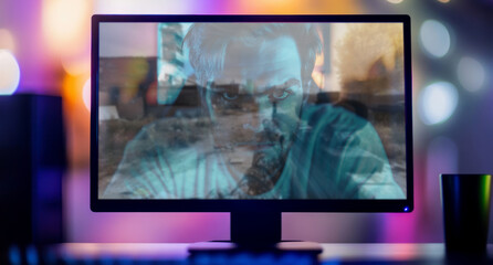 Fototapeta premium Adult gamer plays a shooting computer game, his focused face is reflected in the monitor