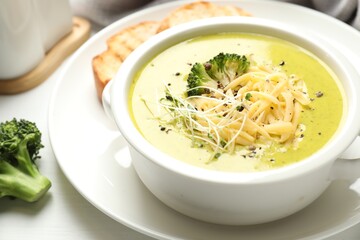 Delicious broccoli cream soup served on white wooden table, closeup
