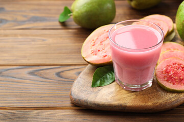 Tasty guava juice in glass, leaf and fruits on wooden table, closeup. Space for text