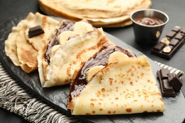 Tasty crepes with chocolate butter and banana on black table, closeup