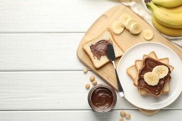 Sandwiches with chocolate butter, bananas and hazelnuts on white wooden table, flat lay. Space for text