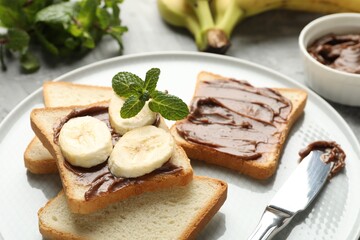 Sandwiches with chocolate butter, bananas, mint and knife on table, closeup