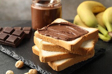 Sandwich with chocolate butter, hazelnuts and bananas on black table, closeup