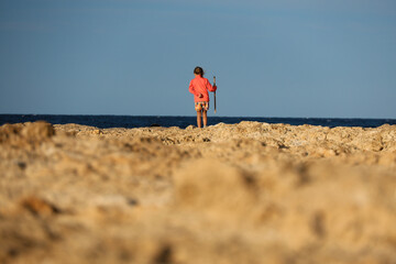 little girl in a bright sweatshirt standing on the edge of a cliff and looking into the sea with a...