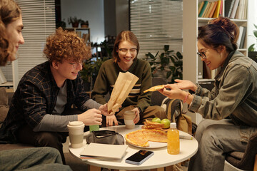 Group of students eating food and enjoying snacks while having fun together in school lounge with low lighting