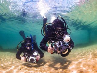 Two scuba divers underwater photographers swimming toward the camera taking pictures in clear water...