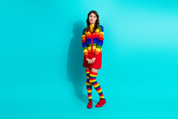 Charming young woman in colorful striped outfit standing against a vibrant turquoise background expressing diversity and freedom