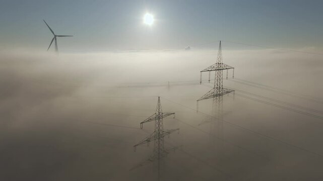 Power pole and wind turbines above the clouds with fog and sun