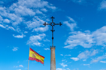 Metal Cross on Stone Pillar with Spanish Flag and Blue Sky