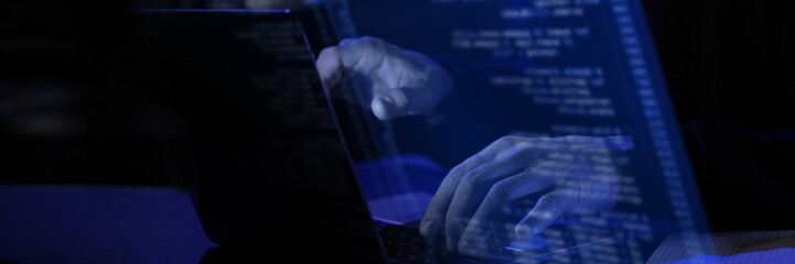 Modern workspace with blue virtual interface displaying fictional programming text. Hands typing on laptop, illustrating cybersecurity, data processing, and futuristic digital concepts.