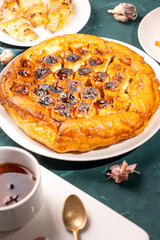 Traditional homemade banana caramel pie. French Tarte Tatin on a white plate with a cup of tea on a green, emerald background. Top view. Close-up.