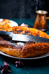 Put a knife on the pie and sprinkle powdered sugar on top to get the contour of the knife on the pie. On a dark background, powdered sugar falls on a banana tart