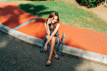 A carefree young woman in a chic summer dress, seated on a vibrant curb, blending minimalist fashion and real estate vibes