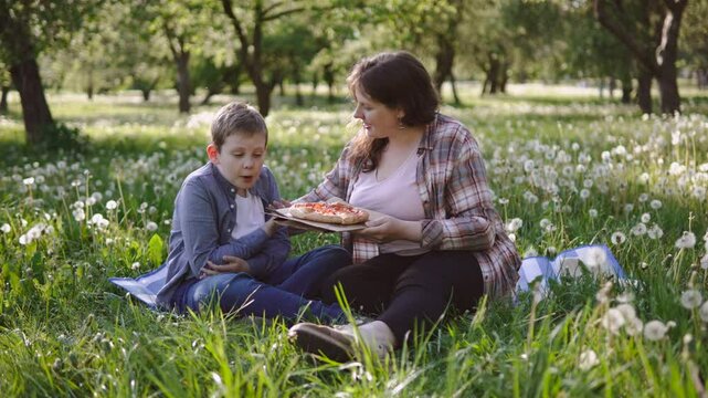 Preteen boy throws tantrum during picnic in park with mother. Parent smiles as talks to boy, child breaks away and becomes indignant. Manifestation of character and stubbornness.