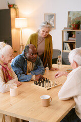 Obraz premium Vertical shot of biracial senior men sitting at table and playing chess while silver headed women watching them