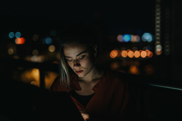 A woman intensely focused on her tablet while working at night, surrounded by blurred city lights,...