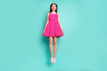 Full size photo of cute lady jumping with toothy smile wearing dotted skirt dress isolated over teal turquoise background