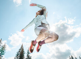 Low angle female athlete jumping against scenic view of blue sky