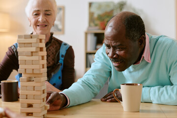 Medium close up of senior Caucasian woman and African American man building high tower of wooden blocks
