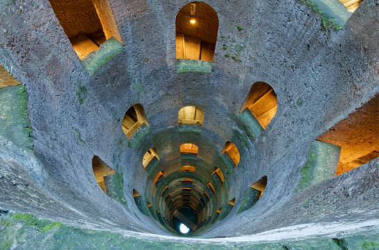 St. Patrick's Well, Pozzo di San Patrizio, view from the top of a deep well with stone steps in spiral form around the sites with lit up archways.