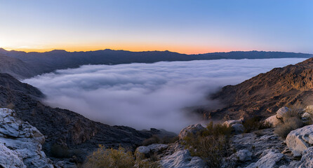 Obraz premium A Sea of Clouds Nestled Between Rugged Mountain Ranges at Dawn, Radiating Serenity and the Beauty of Nature's Majestic Landscape