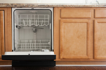 An open dishwasher in a kitchen with wooden fitted units.