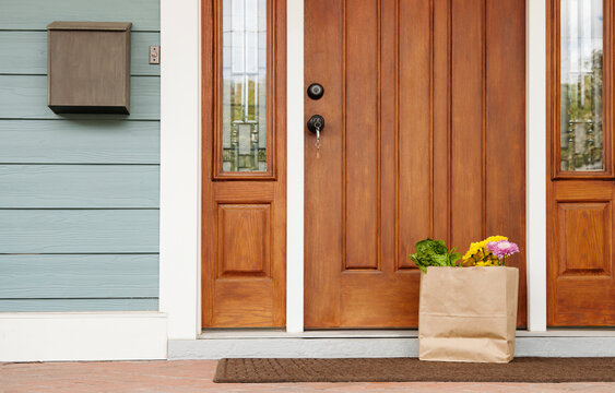 Front door of a house, postbox and a brown bag with flowers and vegetables, Welcome To The Neighbourhood gift.