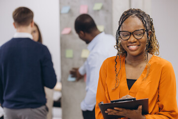 Smiling african american businesswoman holding a folder, diverse professionals collaborating in modern office, brainstorming strategies, sharing insights, driving business innovation and teamwork