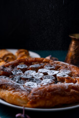 Banana Tarte Tatin is sprinkled with powdered sugar on a white plate on a dark background. The powder is poured onto the cake. Vertical Photo