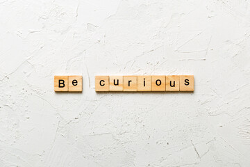 be curious word written on wood block. be curious text on table, concept