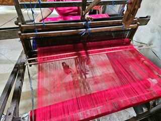 Person weaves vibrant pink fabric on a traditional wooden loom, crafting textiles with skill and...