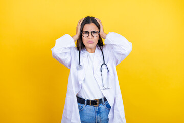 Young brunette doctor woman wearing stethoscope standing over isolated yellow background thinking looking tired and bored with hands on head